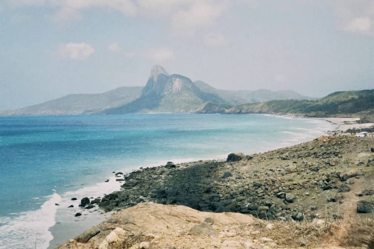 The turquoise sea and rocky shore of Con Son, with the islands' green peaks behind