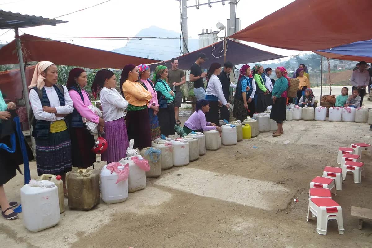 Women from several of the plateau's ethnic groups, each in her own dress, standing beside jerry cans of corn wine at the Dong Van market