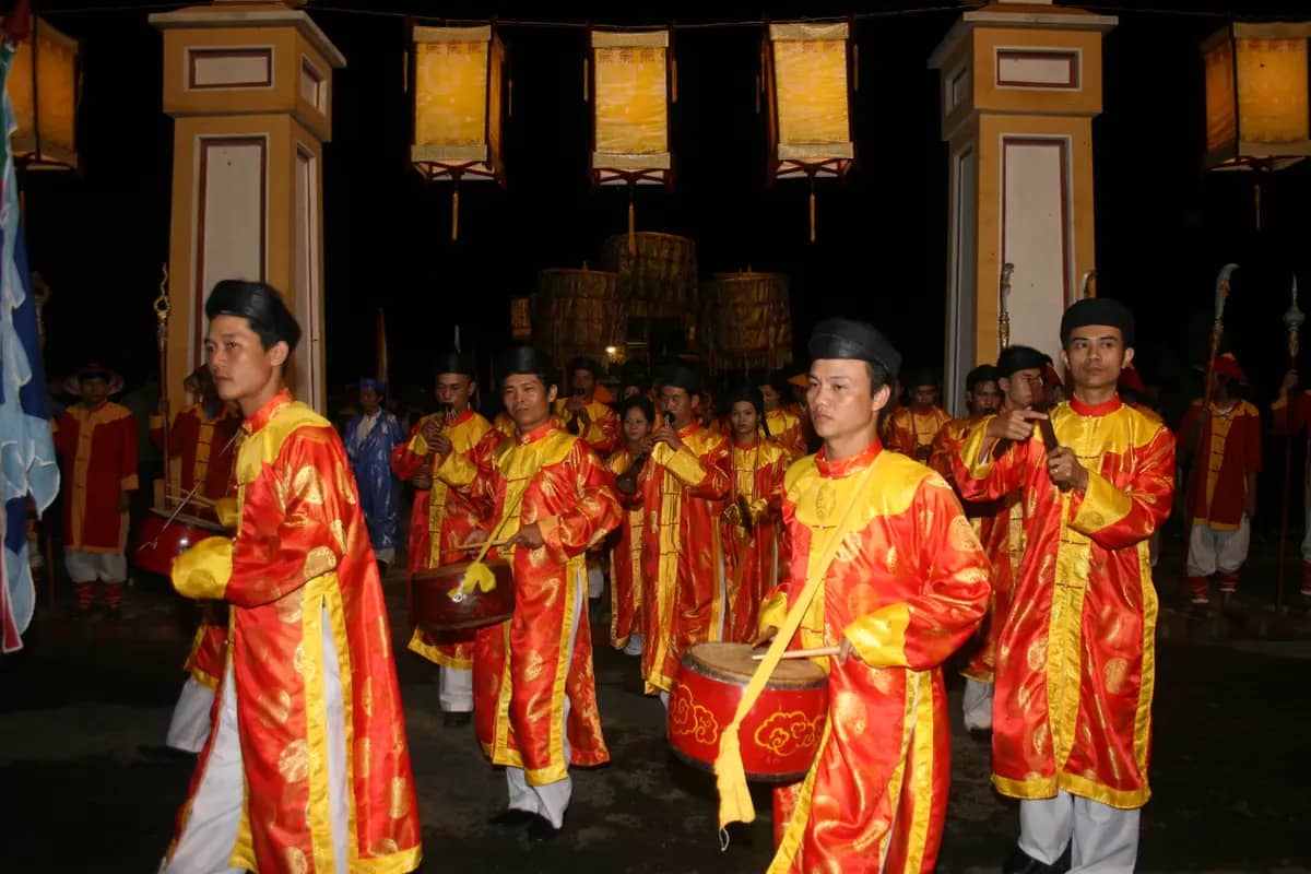 Musicians in red and yellow court robes playing drums and flutes in a nha nhac procession at night in Hue