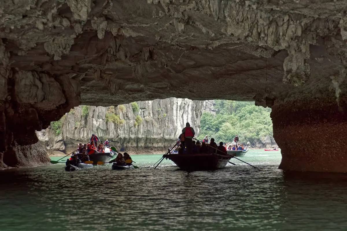 Rowing boats and kayaks passing under the low rock arch of Hang Luon into the enclosed lagoon
