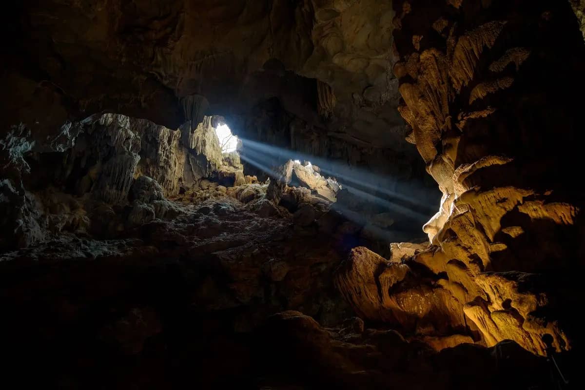 A shaft of daylight falling into the chamber of Dau Go Cave, rock formations lit at the right
