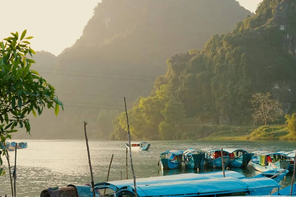 Blue tour boats moored on the Son River at Phong Nha in the evening light, karst peaks behind