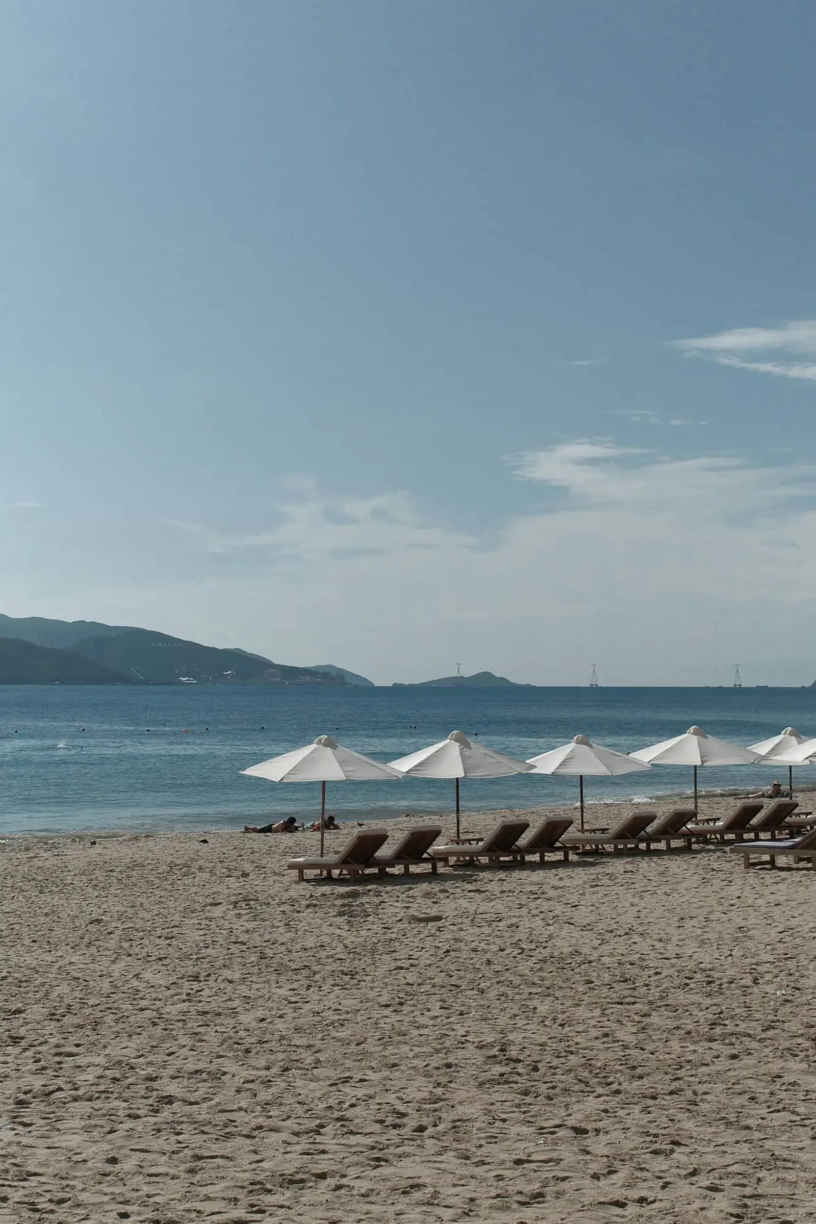 White umbrellas and wooden loungers on the beach by the bay