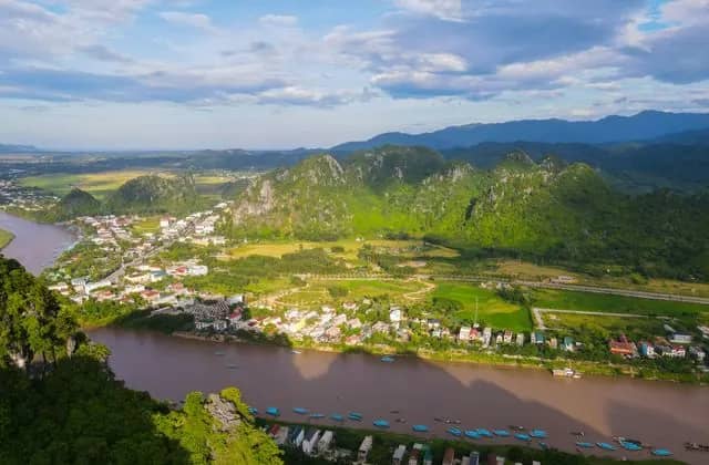 Phong Nha town beside the brown Son River, blue tour boats moored below green karst peaks and rice fields