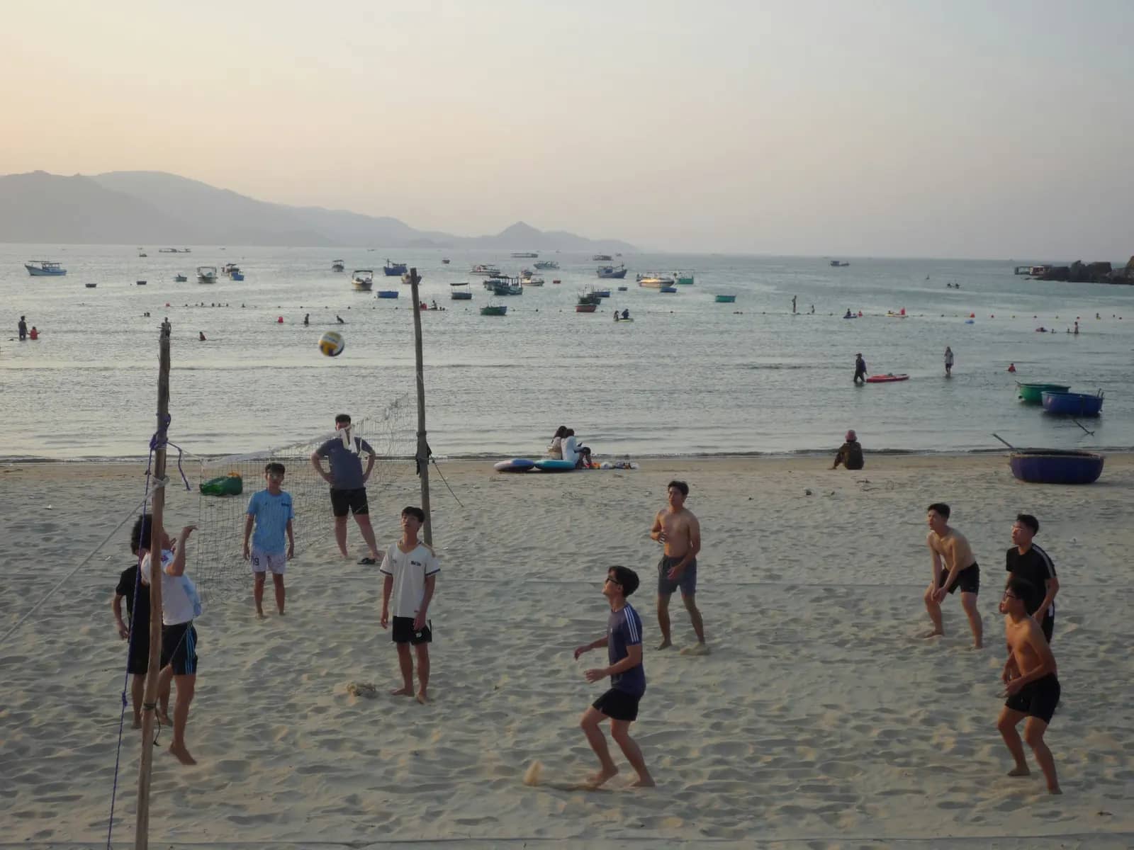 Young men playing beach volleyball, fishing boats offshore