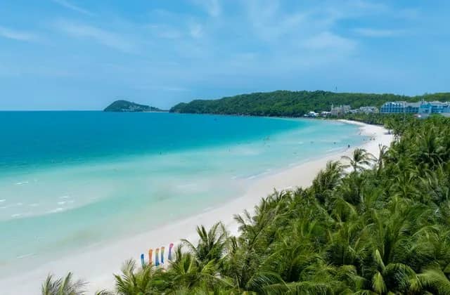 White sand and turquoise water at Kem Beach on Phu Quoc, edged by coconut palms and green hills