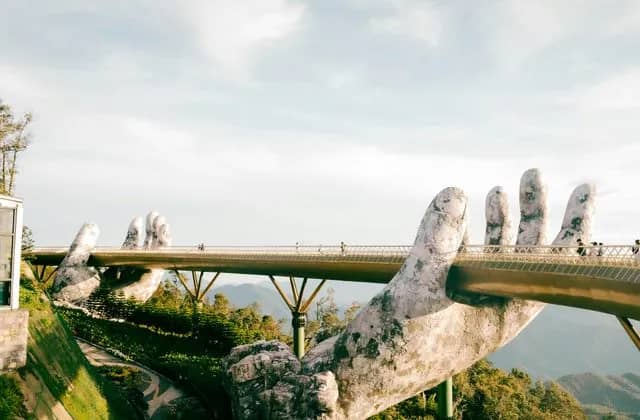 Visitors walk the Golden Bridge on Ba Na Hills, held up by two giant stone hands above green mountains