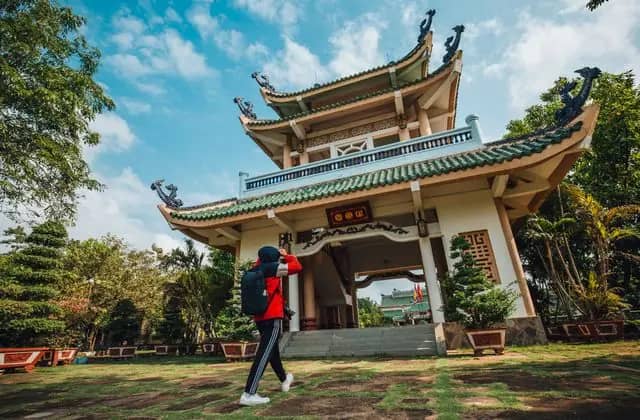 A visitor in a red jacket walks toward the tiered gate of Tran Bien Temple of Literature, Bien Hoa
