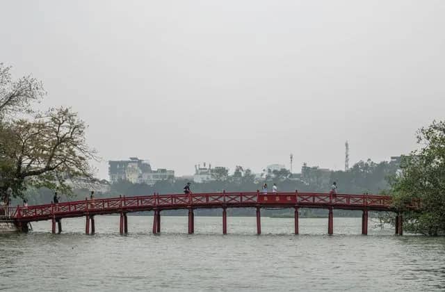 The red The Huc Bridge over Hoan Kiem Lake, the city's towers behind