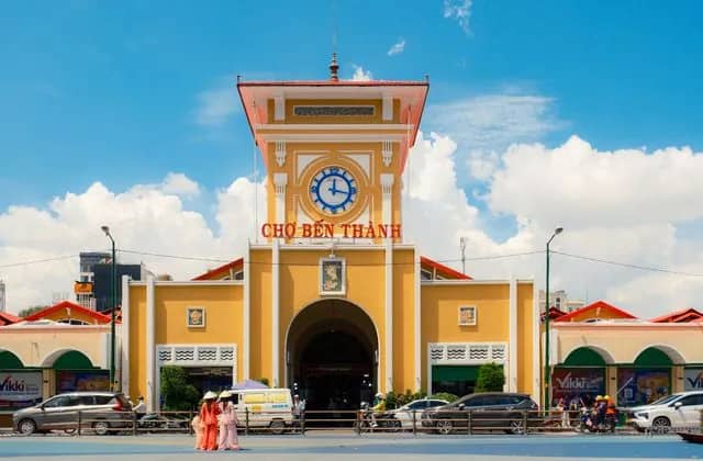 The yellow clock tower of Ben Thanh Market under blue sky, two women in ao dai in front