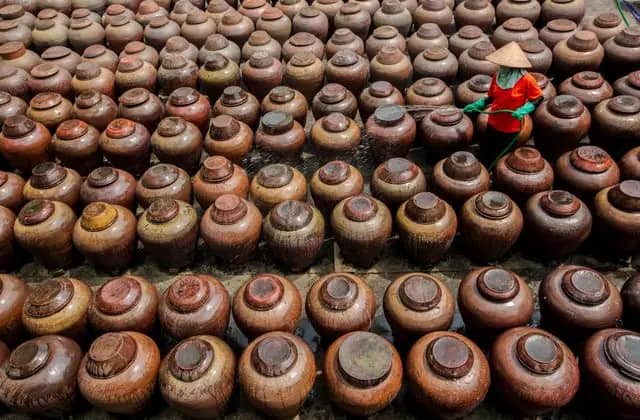 Seen from above, a worker in a conical hat hoses down rows of brown clay jars in Hung Yen