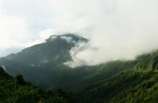 Green forested slopes of the O Quy Ho pass with clouds drifting over a mountain peak in daylight