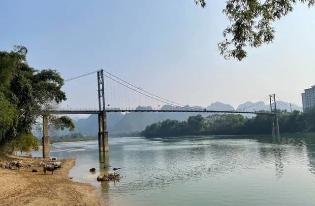 The Khe Ran chain bridge over a river in Con Cuong, forested mountains behind