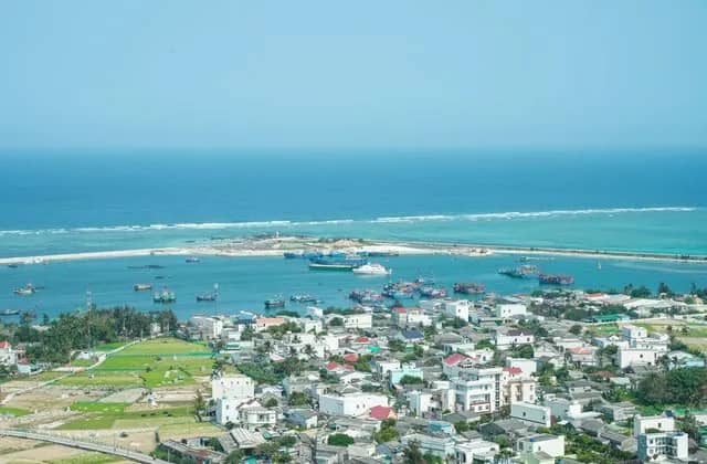 Ly Son Island seen from above, white houses and green fields around a harbour of fishing boats and turquoise sea