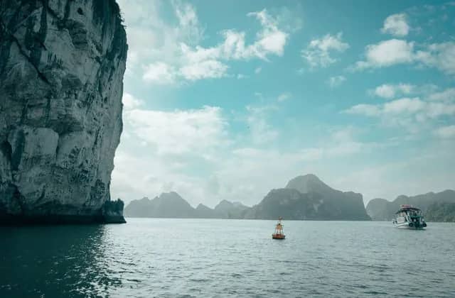 Limestone karsts in the calm water of Ha Long Bay, a boat passing below