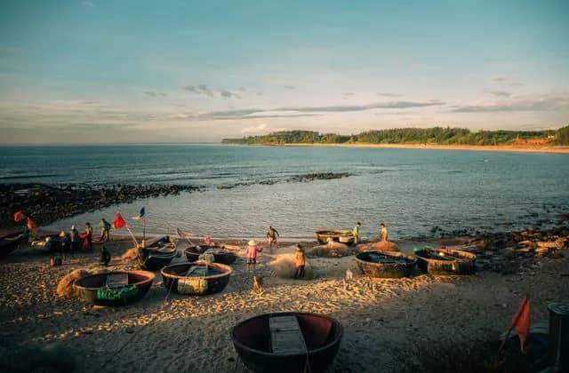 Fishermen sort nets beside round basket boats on the sand at Cua Tung beach in warm evening light