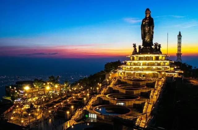 The giant Buddha statue on Ba Den Mountain lit at dusk above the city lights