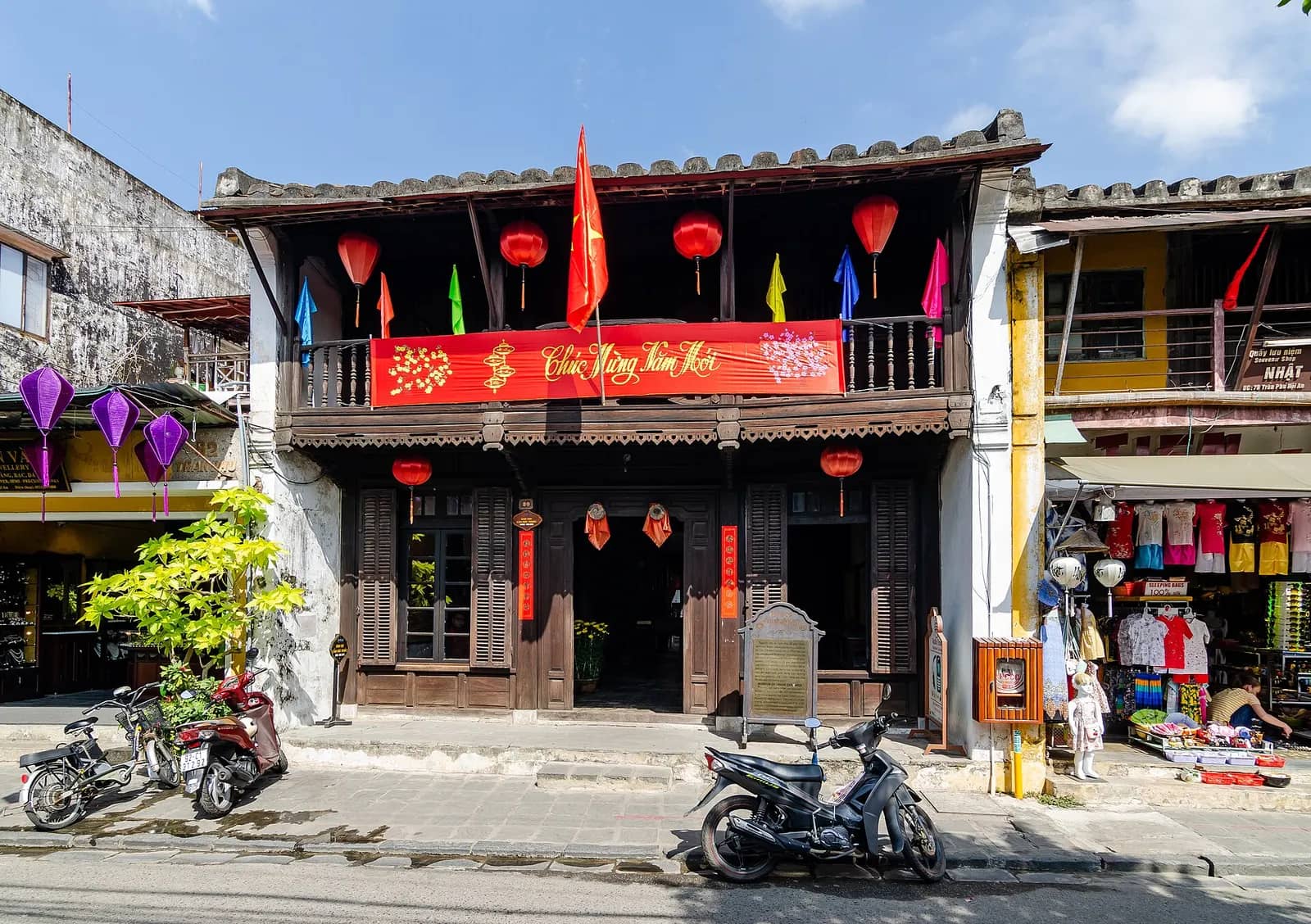 The two-storey wooden front of the Museum of Trade Ceramics on Tran Phu Street, with a balcony, red lanterns and flags and motorbikes parked outside