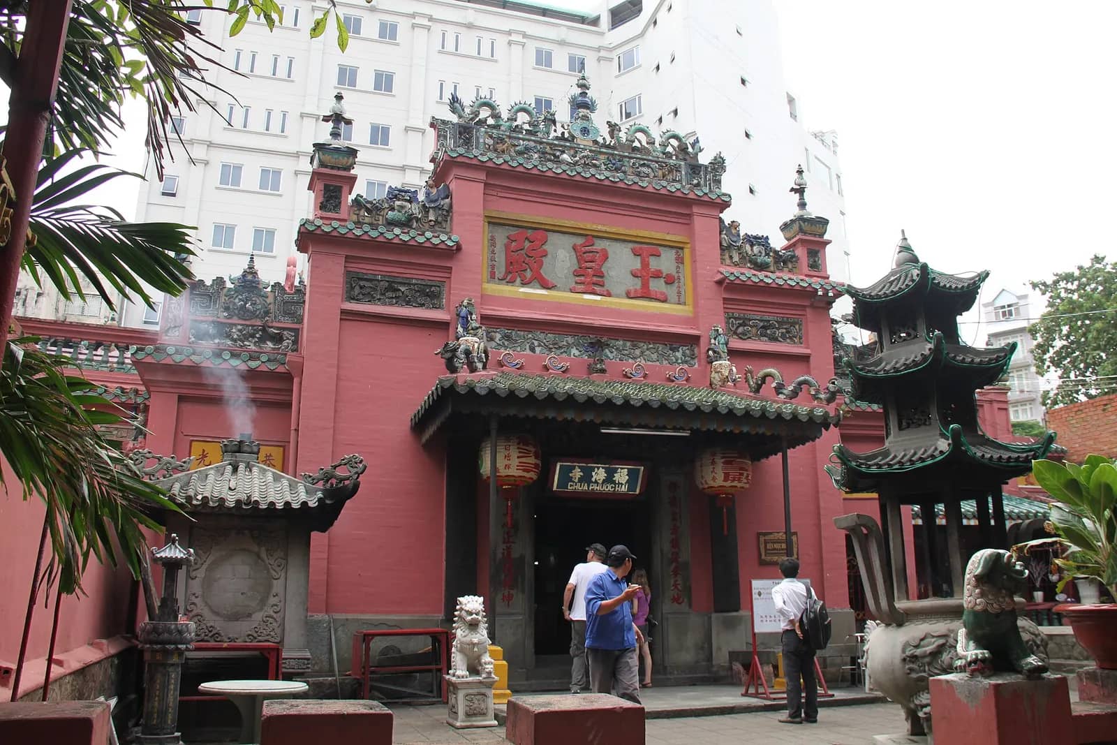 Red front of the Jade Emperor Pagoda with gold Chinese characters, incense smoke and a tiered stone tower in the courtyard