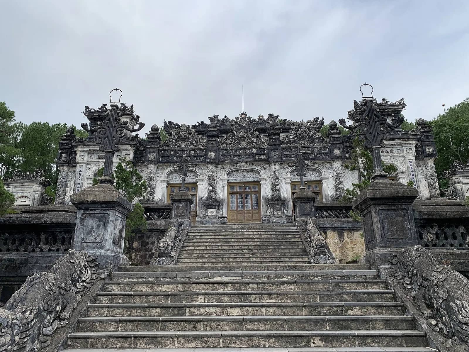 Steep stone stairs at Khai Dinh Tomb rising between carved dragon balustrades to a grey, heavily ornamented hall