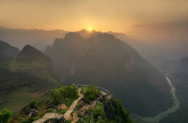 Sun rising through layered mountain ridges in Ha Giang, seen from a cliff-top path