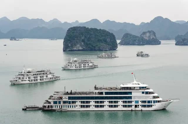 Cruise boats gliding between limestone islands in Ha Long Bay under a hazy sky