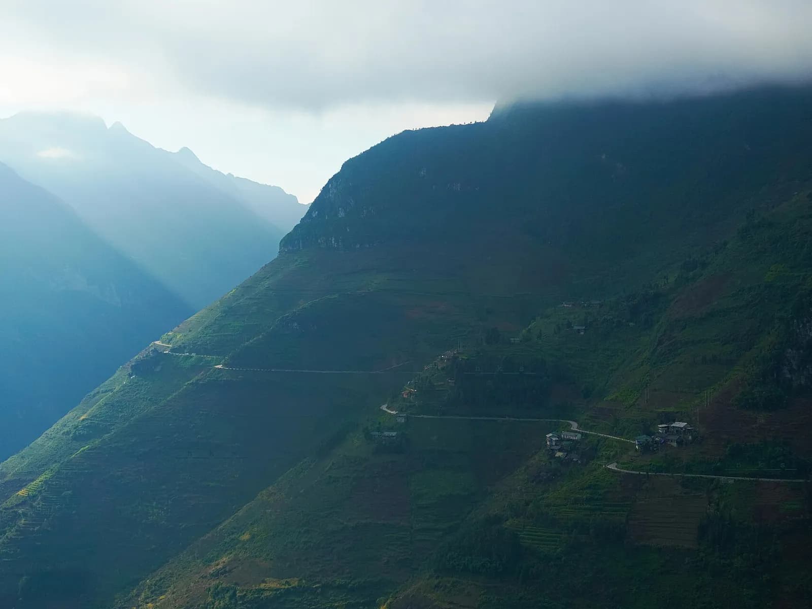 Cloud sitting on the steep green ridges of the Ma Pi Leng pass in Ha Giang, a road cut into the slope
