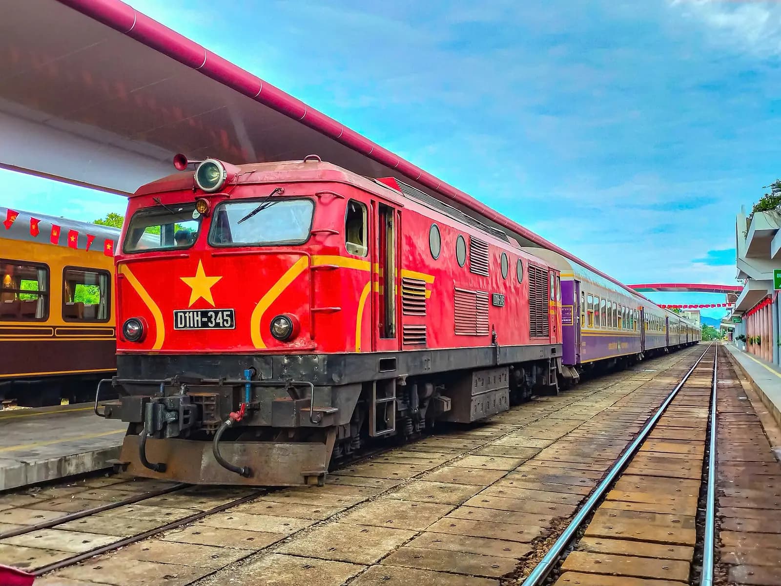 A red diesel locomotive with a yellow star waiting beside the platform at Hue station with its carriages