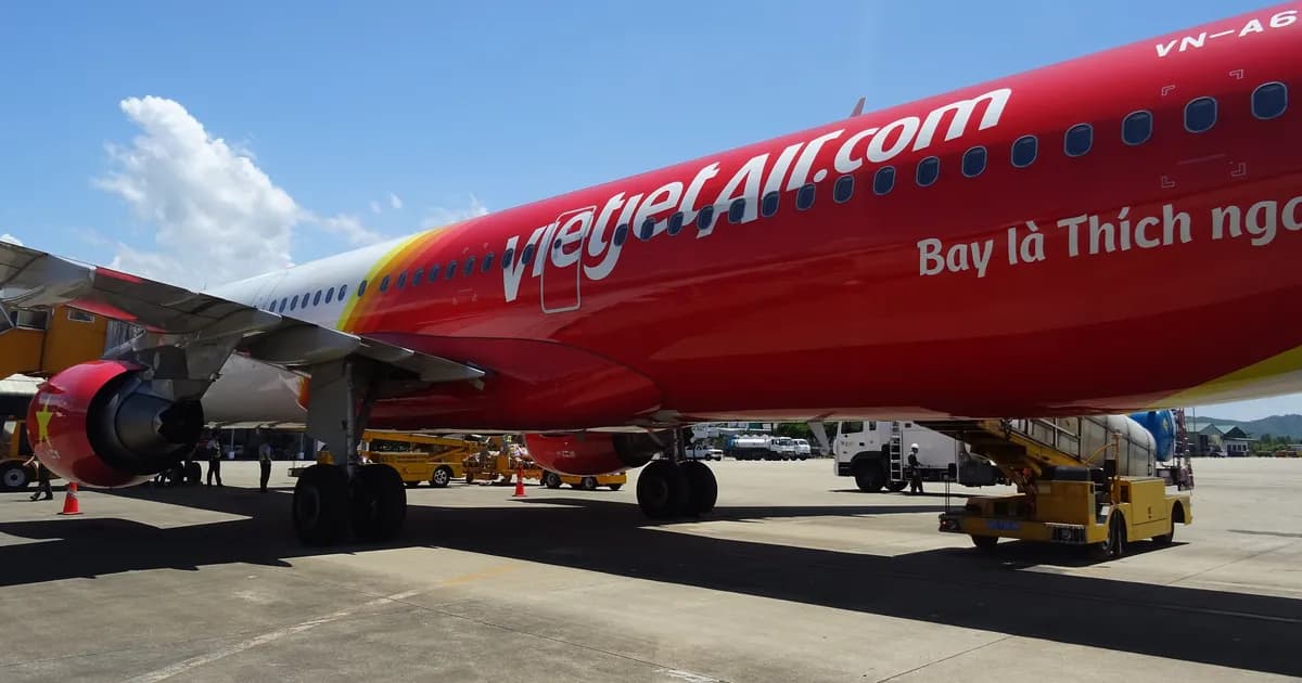 A red and white Vietjet Air jet parked on the apron at Phu Bai airport near Hue, ground equipment beside it