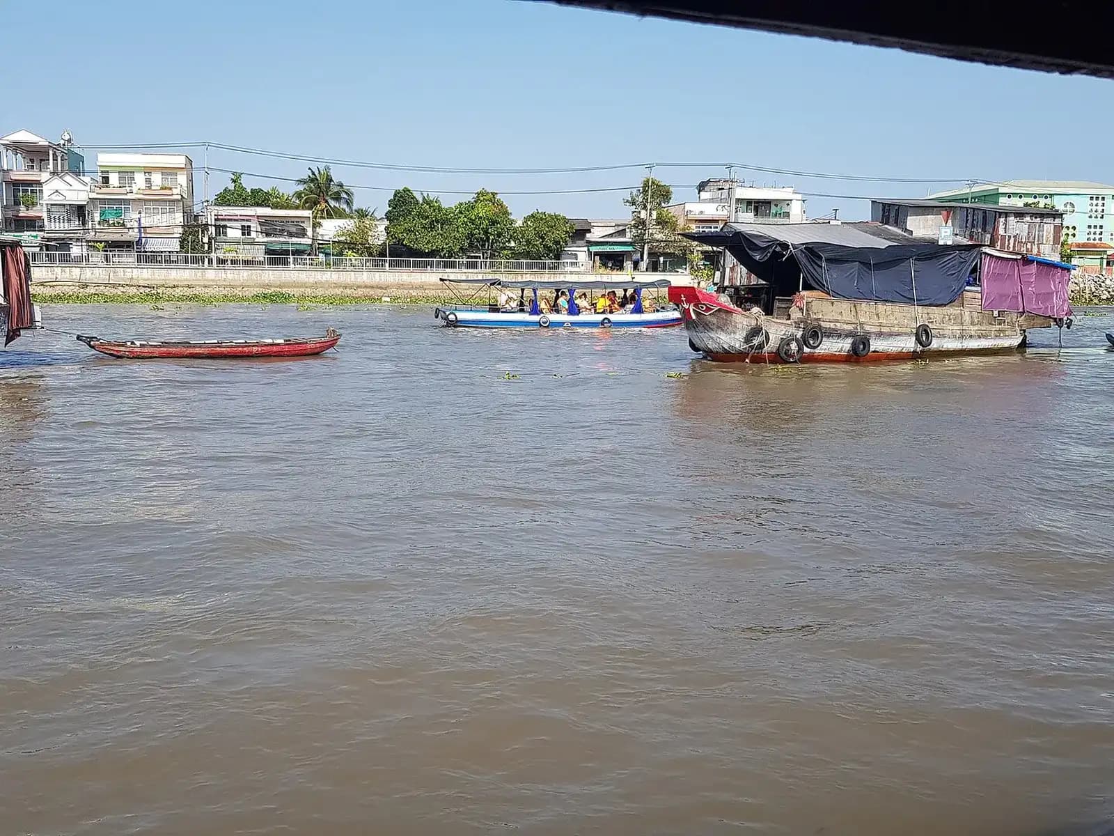 Boats and a covered houseboat on the brown water of a floating market in Can Tho