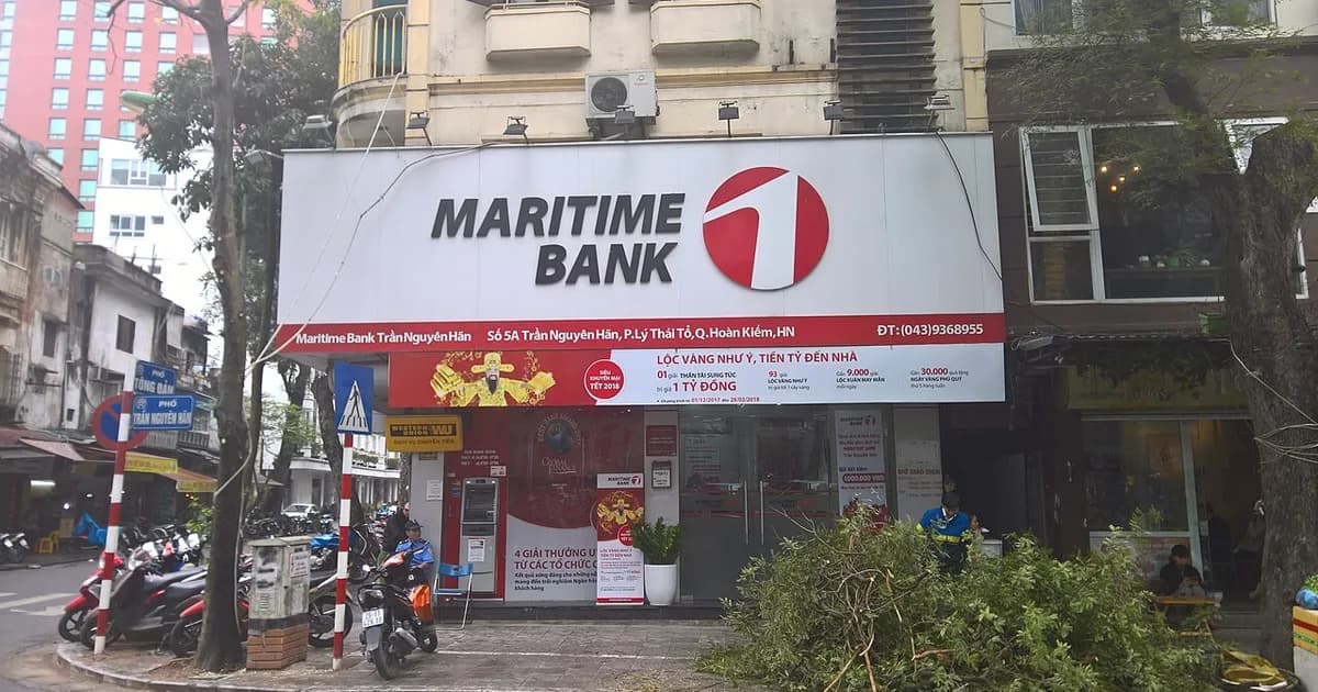 A Maritime Bank branch with a large red and white sign on a tree-lined Hanoi street, motorbikes parked outside