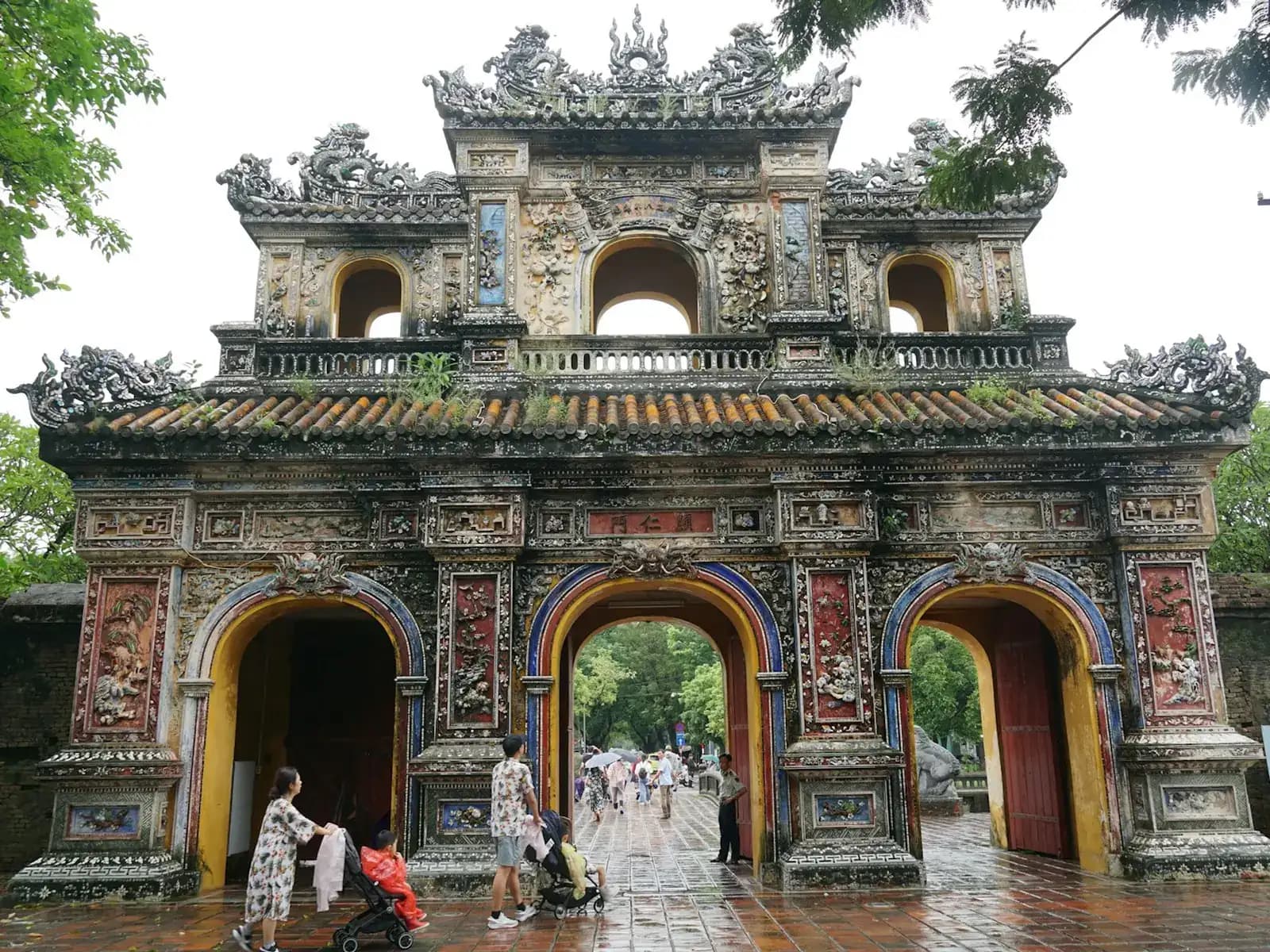 Visitors with a stroller passing through the ornate Hien Nhon Gate of the Hue Imperial City on wet paving