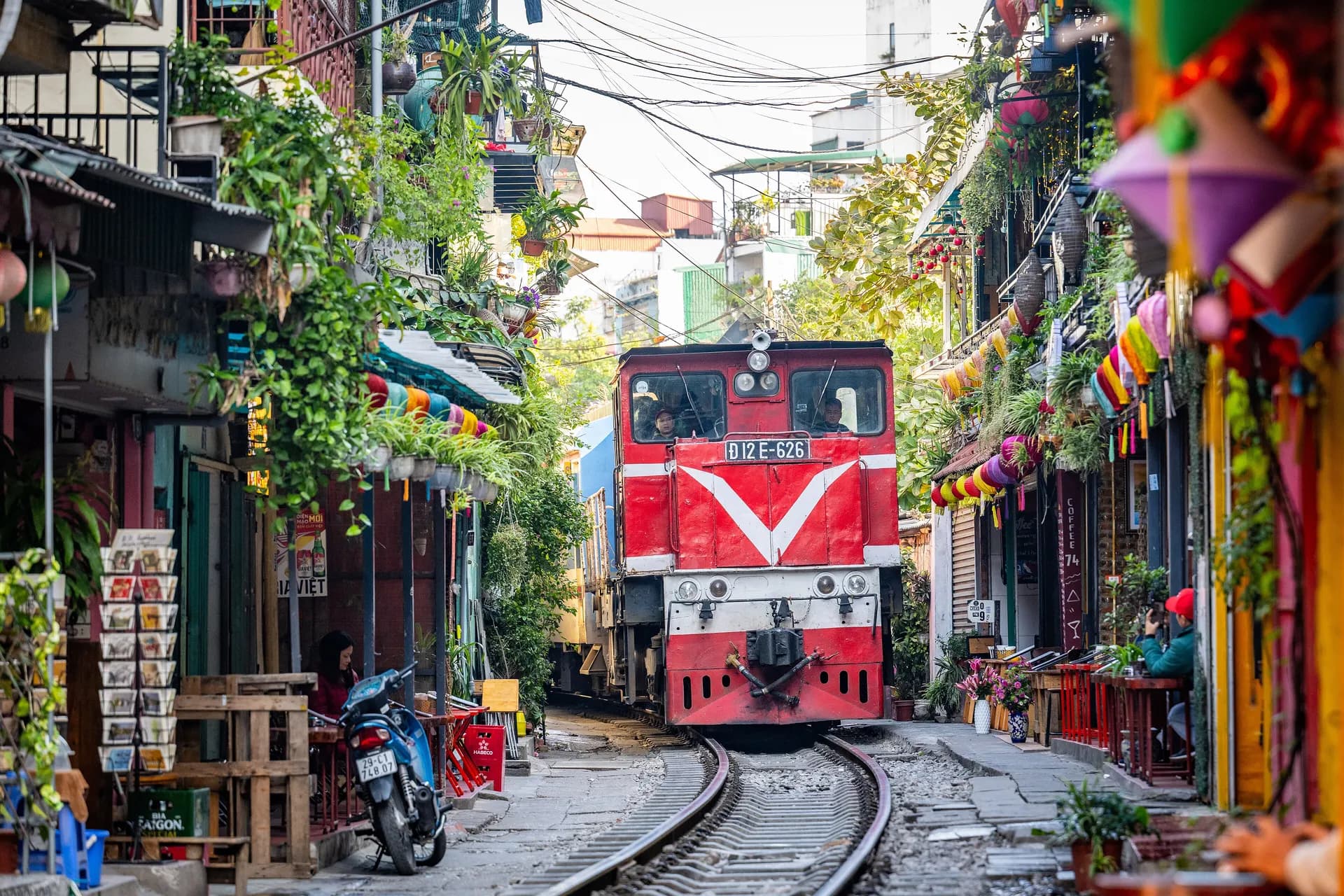A red diesel train rolling down the narrow Hanoi Train Street between colorful houses
