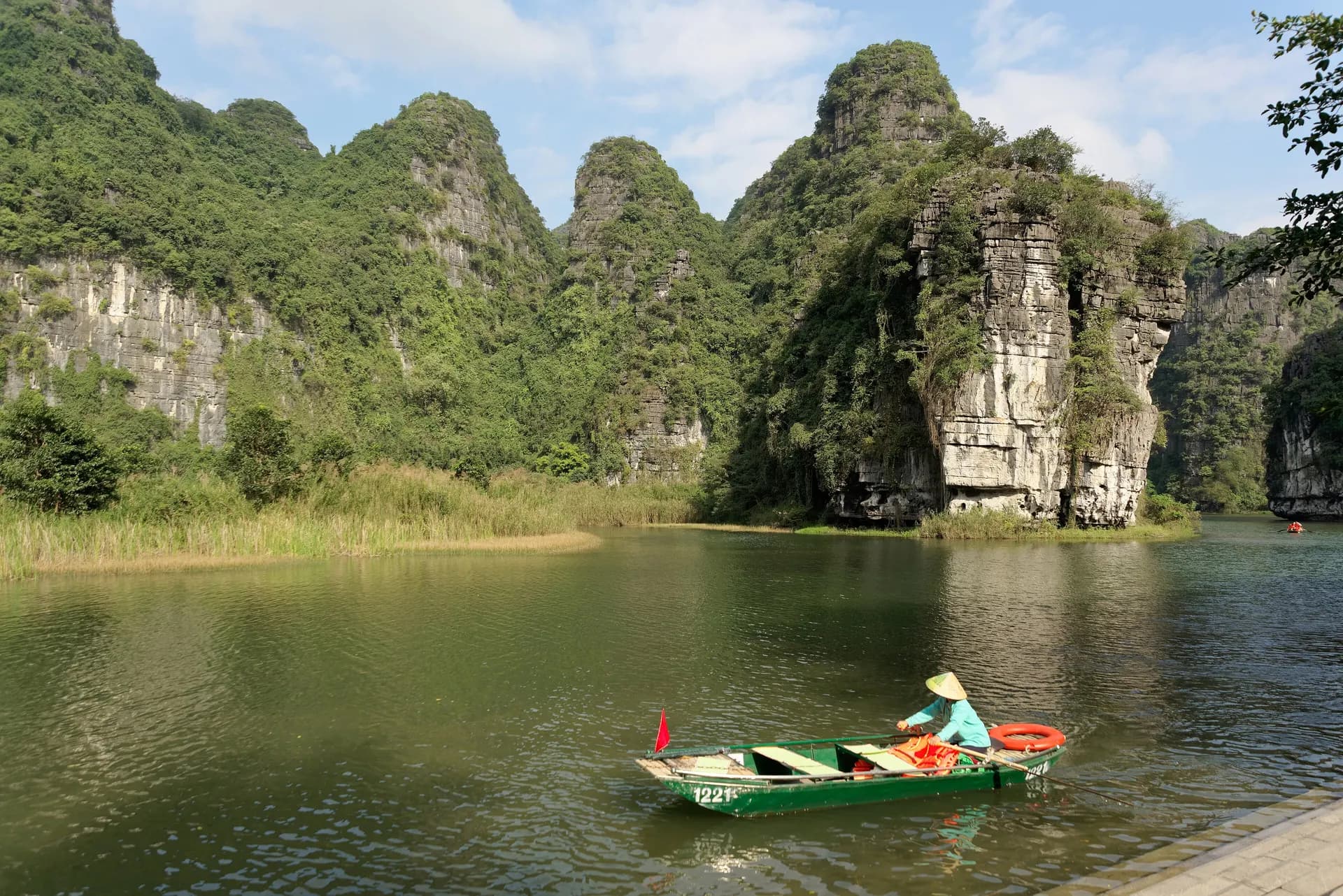 A rower guiding a small boat across a calm lake below limestone peaks in Ninh Binh