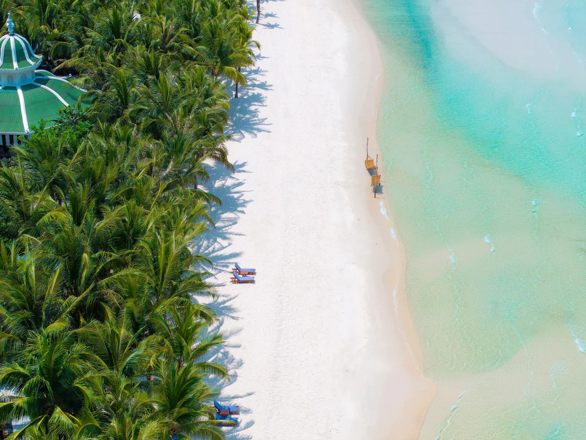 Aerial view of a white sand beach and turquoise shallows fringed by palms on Phu Quoc