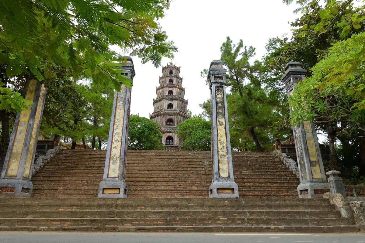 Brick steps and four stone pillars leading up to the seven-storey Phuoc Duyen tower of Thien Mu Pagoda, framed by trees