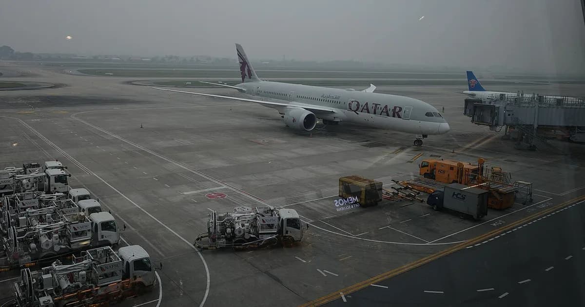 A Qatar Airways jet on the apron at Hanoi's Noi Bai airport, fuel trucks and baggage carts in the foreground on a hazy day
