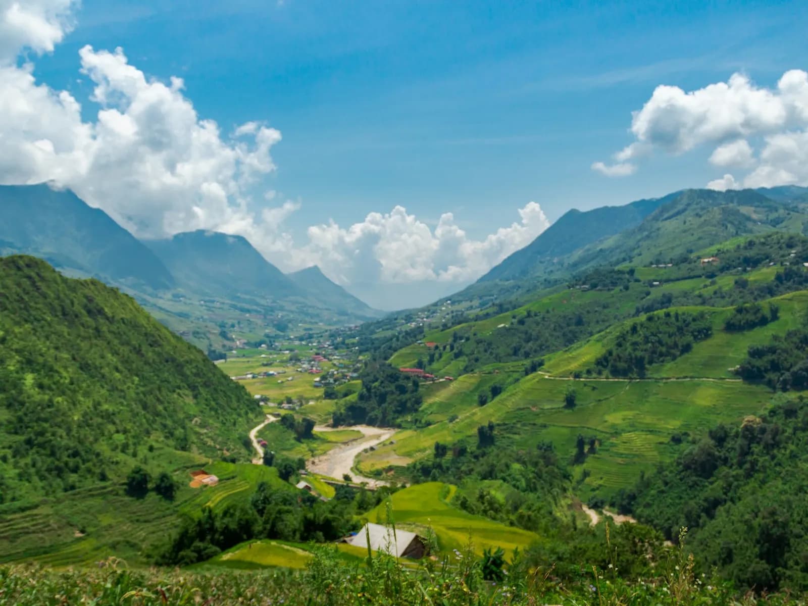 A green valley near Sa Pa with a river and road below steep forested mountains and white clouds