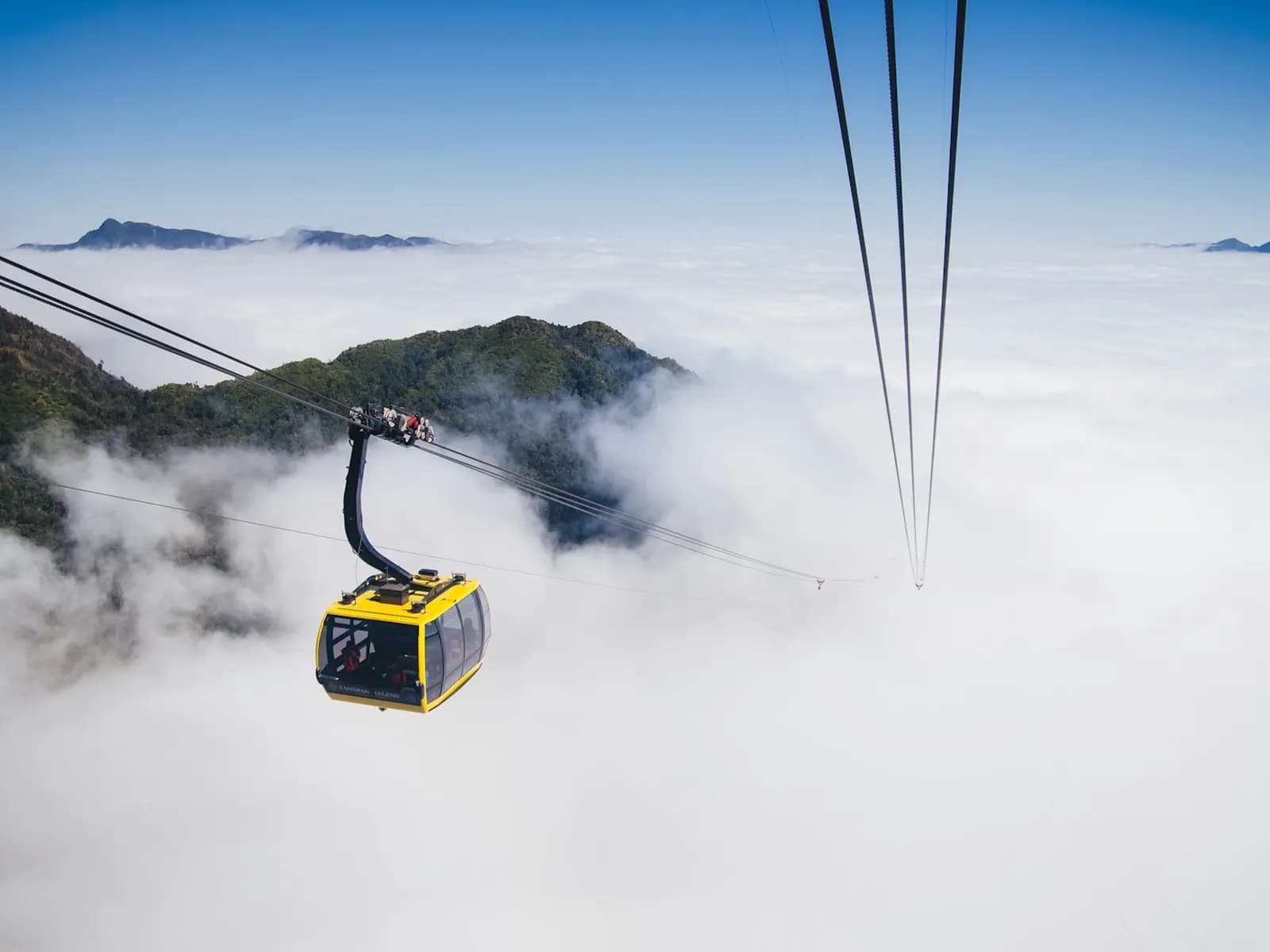 A yellow Fansipan cable car cabin gliding over a thick sea of cloud, with mountain ridges poking through