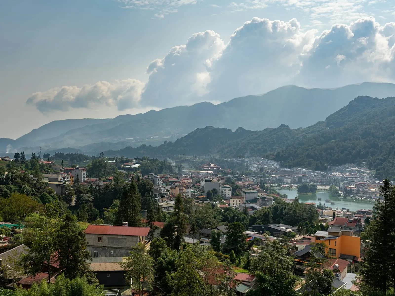 Sa Pa town and its lake spread across a green valley, with tall clouds building over the mountain ridges