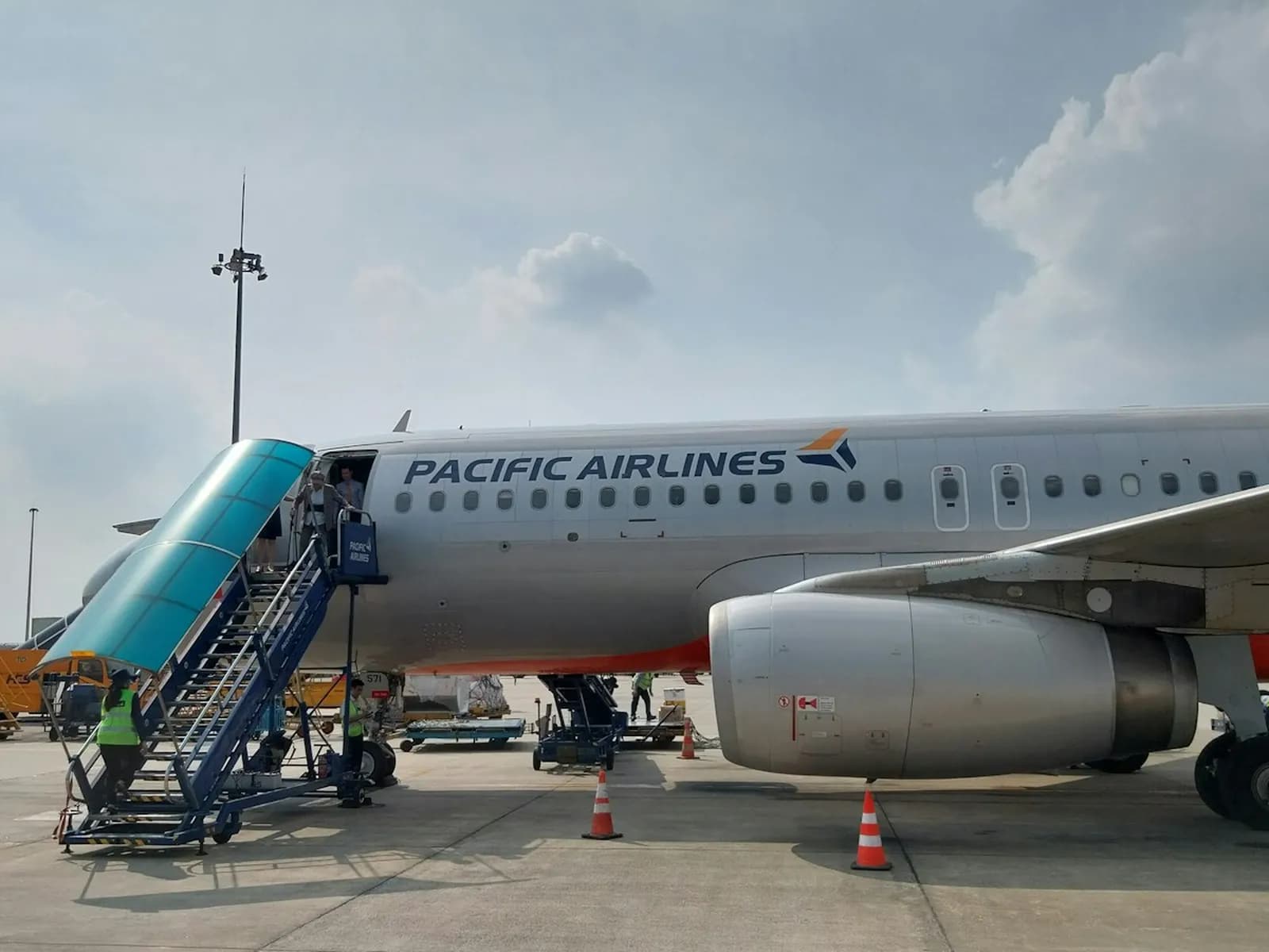 A Pacific Airlines Airbus A320 parked at Noi Bai airport with boarding stairs and ground crew beside it