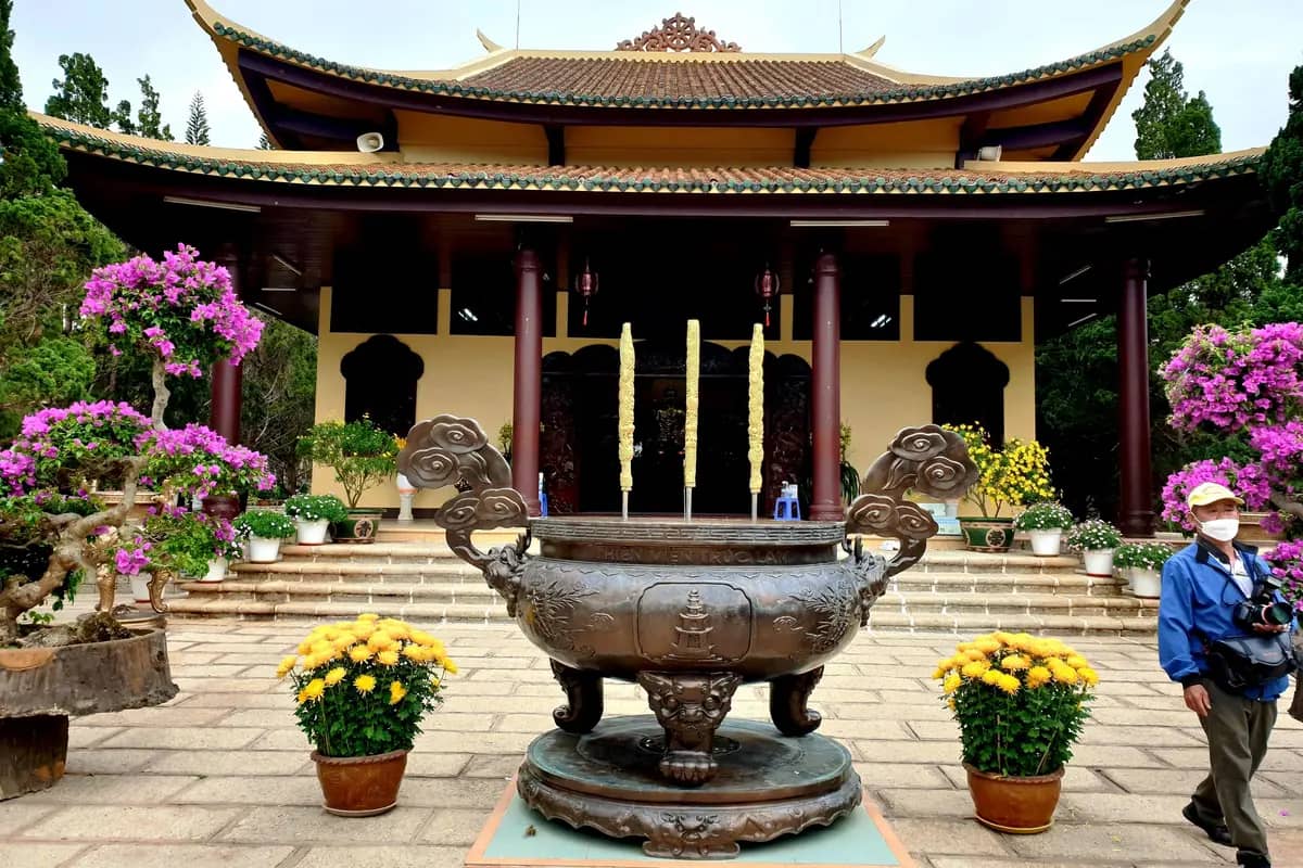 The main hall of Truc Lam monastery, a bronze incense urn and pots of flowers in front