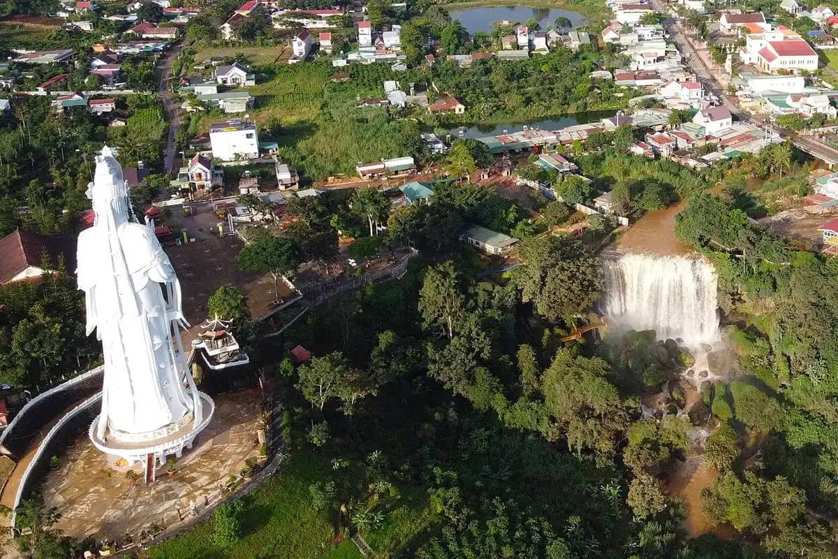 The tall white statue at Linh An Pagoda with Elephant Falls beside it, seen from the air