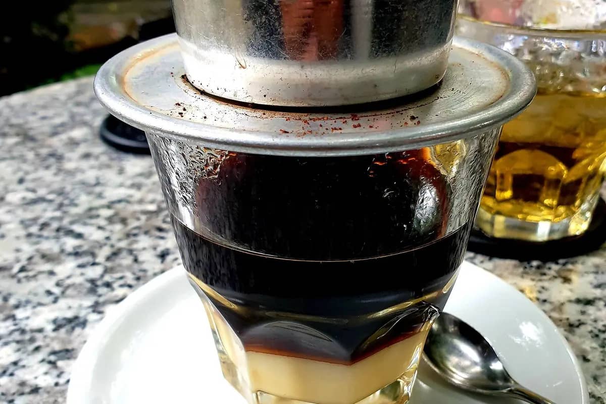 Coffee dripping through a metal phin filter into a glass with condensed milk at the bottom