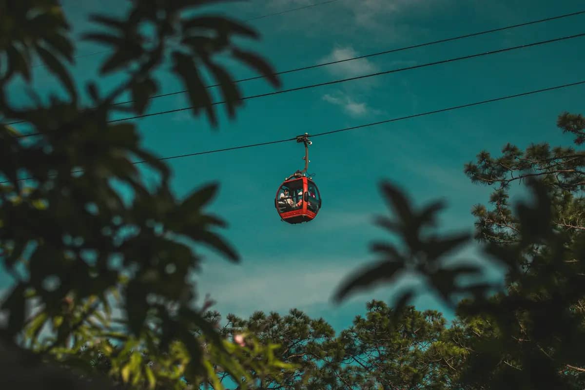 A red cable car cabin passing over the pine trees in Da Lat
