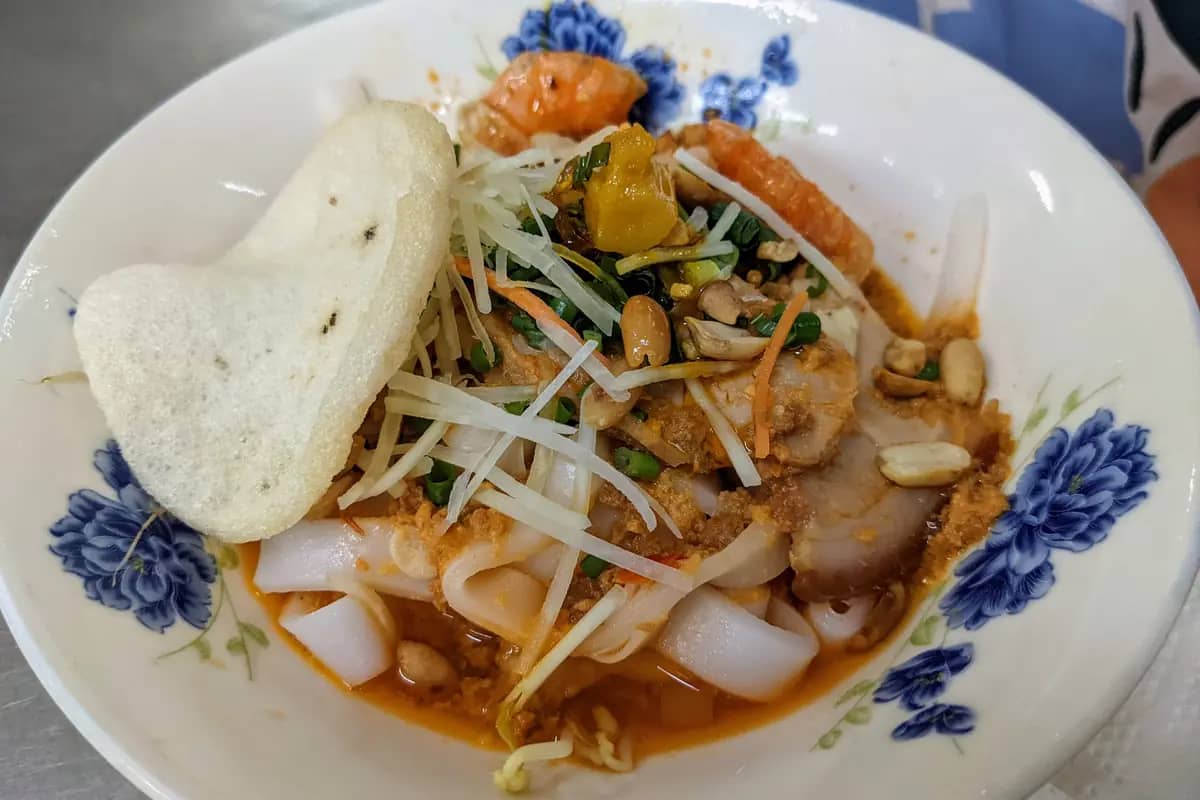 A bowl of mi Quang with pork, shrimp, peanuts and a sesame rice cracker