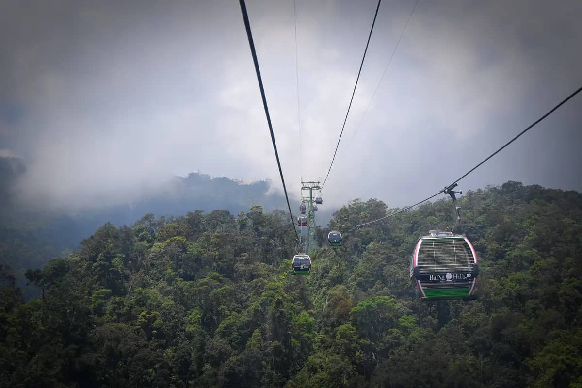 Cable car cabins gliding over the forest below Ba Na Hills, cloud hanging over the slopes