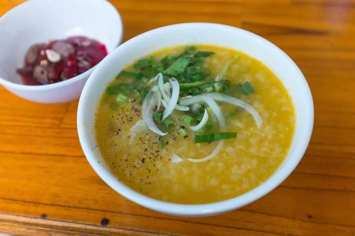A bowl of rice porridge with spring onion and black pepper in Da Nang, a dish of duck blood jelly beside it