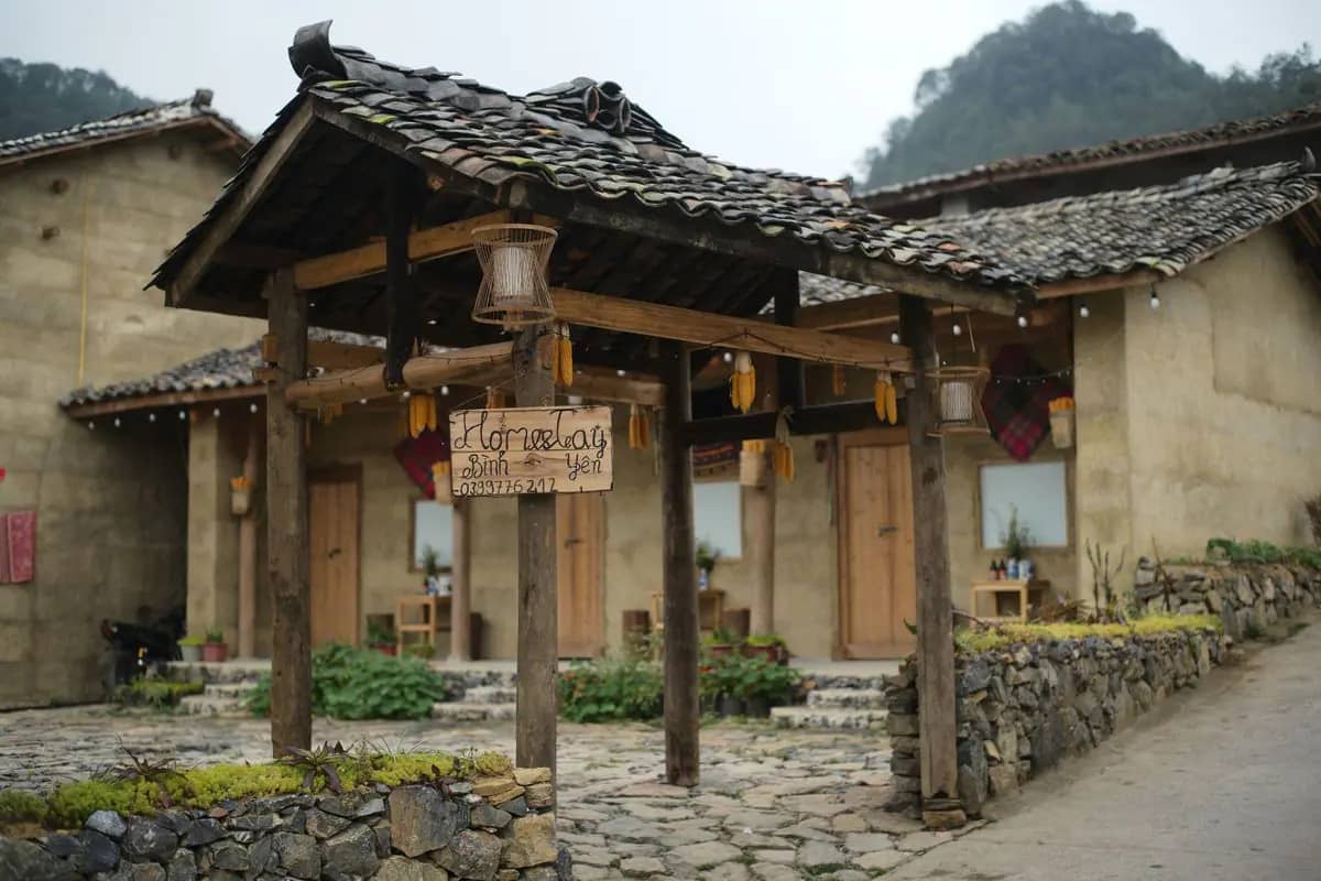A homestay of earth-walled houses with a wooden gate and stone paving at Lo Lo Chai village