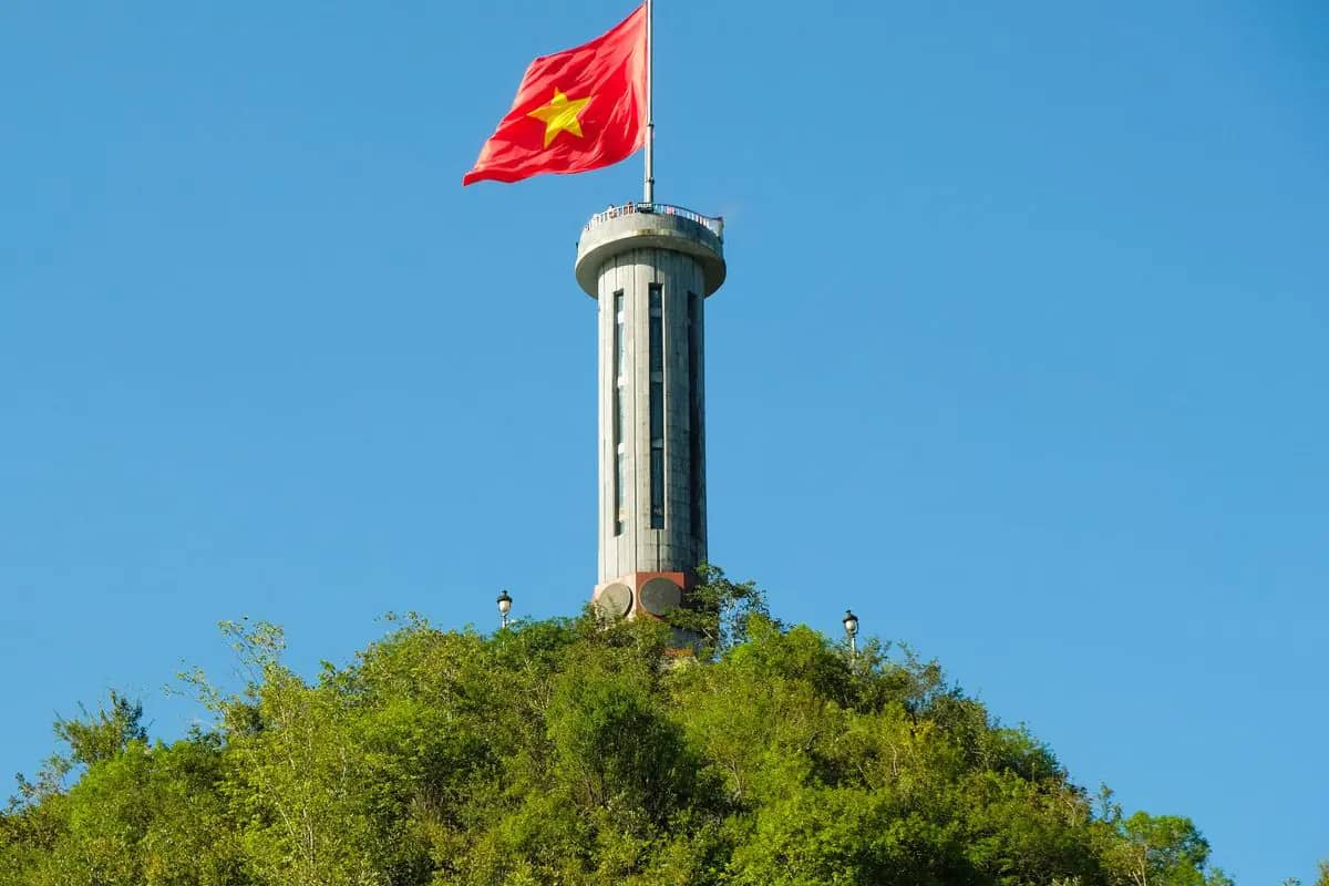 Lung Cu flag tower on its wooded peak, a large Vietnamese flag flying from the top under a blue sky